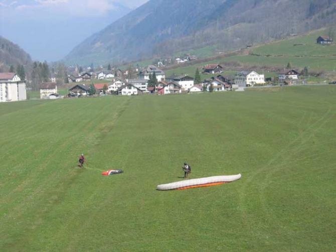 Linthal: gelandet. Das Landefeld erstreckt sich bis zu den Häusern weiter hinten; rechts wird der Landeplatz durch eine Strasse, links durch die Linth und den Sportplatz begrenzt.