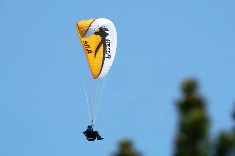 Gleitschirmflieger gleitet durch die Luft, mit einem weiß-gelben Baldachin-Flügel