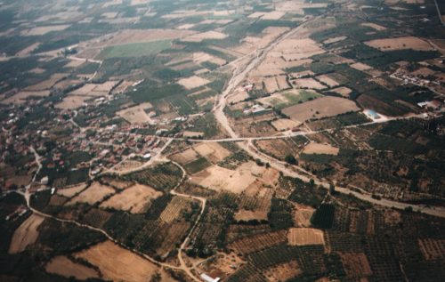 Links der Ort Sikourio, quer durchs Bild die Strasse von Elatia nach Sikourio und Ossa. Der große L-förmige Acker mit dem einzelnen Baum drauf,  vor der Brücke über das trockene Flußbett kann im Herbst als Landeplatz genutzt werden.
Bild: Womble 1995