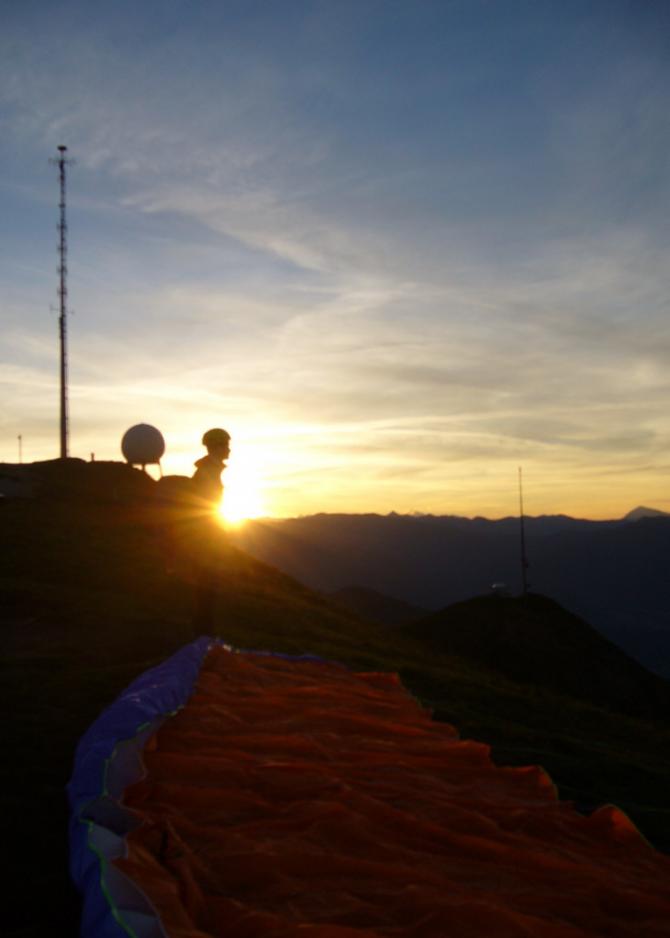 Patrick bei Sonnenaufgang am Startplatz des Monte Lema. Es ist kalt und windig, wie's halt um 5:30 Uhr auf einem Gipfel so ist. Zuvor in der Dunkelheit hochgelaufen, viel zu früh oben angekommen, in der Kälte auf den Sonnenaufgang gewartet und gefroren... Zumindest hats schöne Fotos und ein gemütliches Flüglein gegeben.