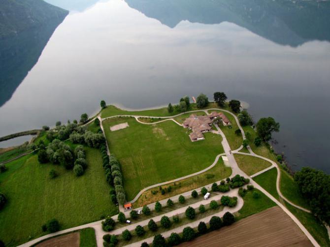 Hab mir den Landeplatz Anfang August 2015 vom Klettersteig aus angeschaut. Ringsrum Bäume, Richtung See Fahnenmasten und kleine Sträucher/Bäume -> mit dem Drachen praktisch nicht anfliegbar. Bei Null Wind zu klein, bei Talwind Verwirbelungen. Bild von: http://www.mountainzones.com/2012/06/07/bergseeidyll-und-adrenalinstoss-im-stundentakt-geht-das-klar-am-idro-see-kettern-gleitschirmfliegen-und-kulinarische-genuesse-inclusive/